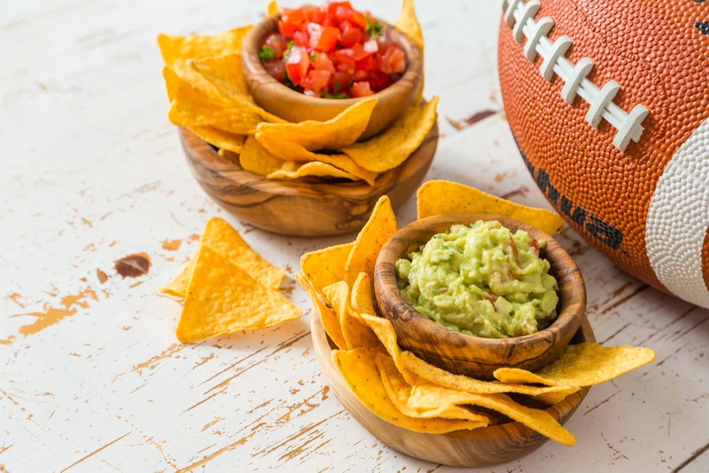 Guacamole and salsa served with chips next to a football 